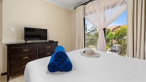 Ein Hotelzimmer mit Bett, Fernseher auf einer Kommode und Blick auf Palmen sowie ein Auto durch das Fenster.