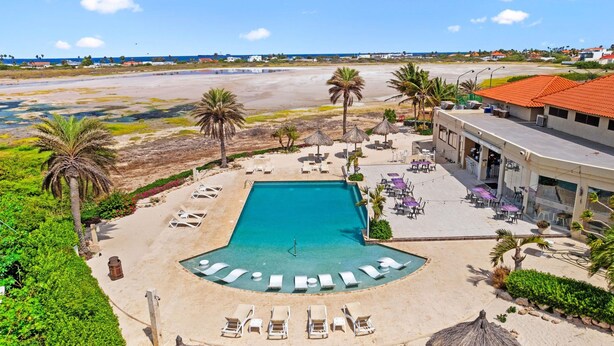 Ein Resort mit einem zentral gelegenen Schwimmbad, Liegestühlen und Strandabschnitt.
