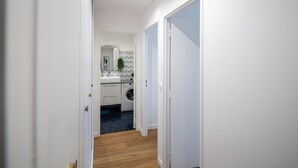 Un couloir menant à une cuisine équipée d’un lave-linge et dont le mur derrière l’évier est recouvert de carreaux.