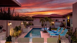 A pool area with lounge chairs, a small pool, and a sunset view.