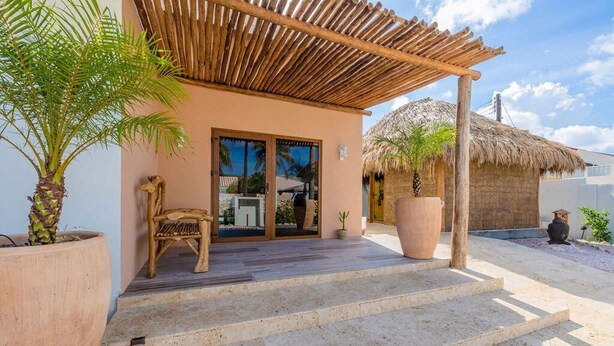 A building with a covered porch, a thatched-roof structure, and potted plants. - Buddha House 5 5 Palapa Suite Pool in Palm Beach (Noord)