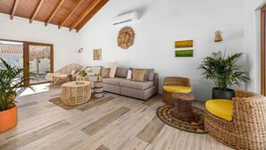 A spacious living area with a high ceiling, a grey sofa, wicker furniture, and a large window. - Buddha House 5 5 Palapa Suite Pool in Palm Beach (Noord)