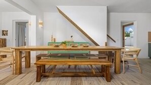 A dining area with a long wooden table, benches, wicker chairs, and a green console table with decorative items. - Buddha House 5 5 Palapa Suite Pool in Palm Beach (Noord)