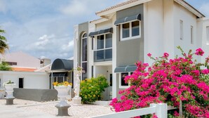 Une maison à deux étages avec un balcon, une véranda et un jardin agrémenté de fleurs roses.