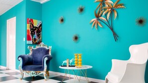 Une pièce aux murs de couleur turquoise, avec un sol à carreaux noirs et blancs, un fauteuil bleu, un fauteuil blanc et une petite table blanche agrémentée d’objets décoratifs.