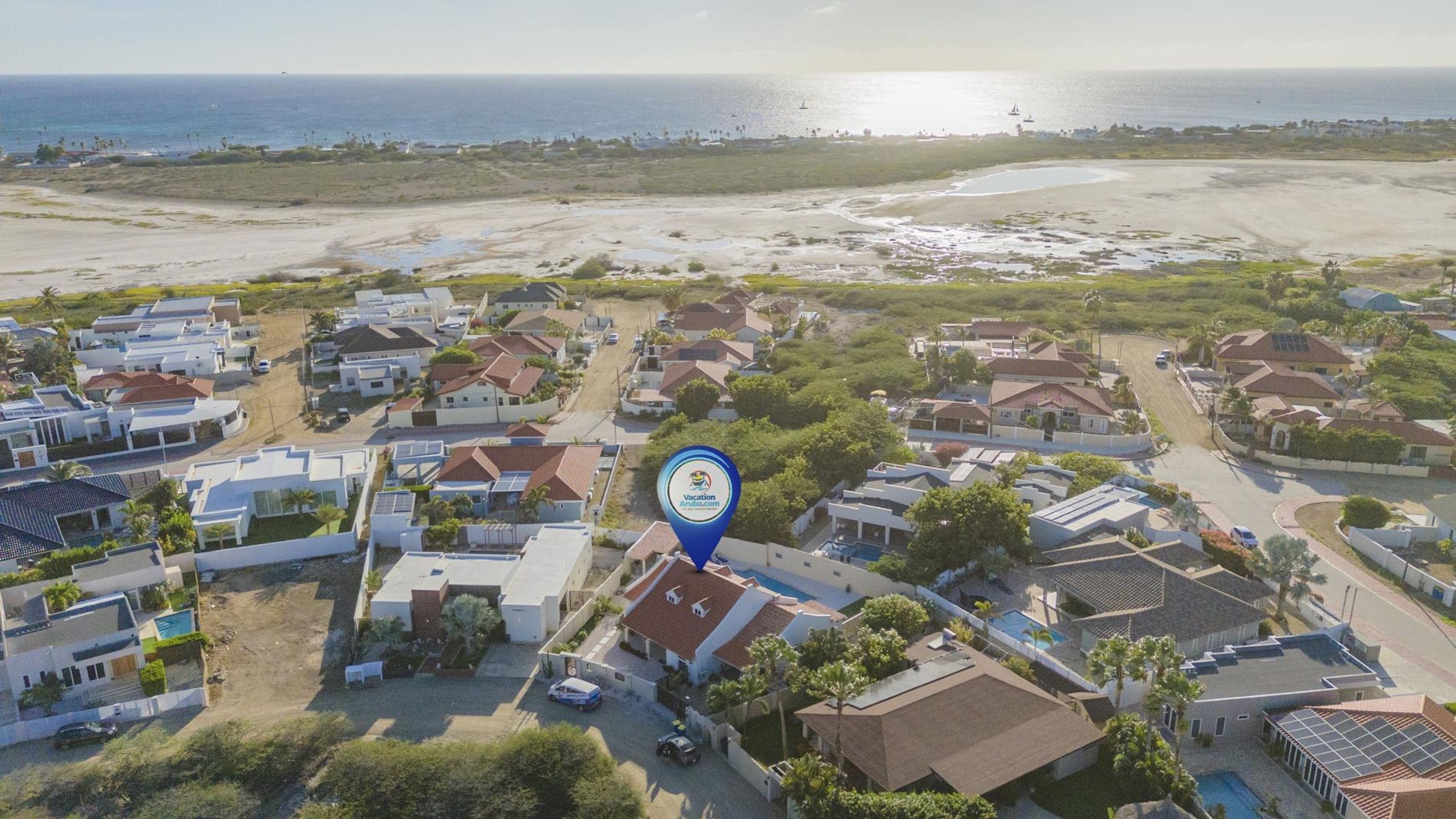 An aerial view of a residential area with houses, a beach, and a body of water.