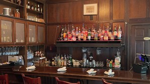 Zona de bar con paneles de madera, una variedad de botellas de licor y taburetes.
