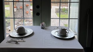Un comedor con una mesa dispuesta para dos personas, que incluye dos platos y cuencos blancos, un tarro pequeño y cubiertos.