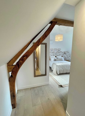 A bedroom with a wooden staircase, a large mirror, and a bed with a white duvet. - Résidence CH-MAISONS (Cricqueboeuf)