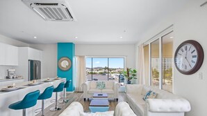 A modern living room with a sofa, two ottomans, a coffee table, and a bar area with blue bar stools. - Lux Palm Beach Escape Pool Gym Prime Location (Noord)