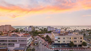 Un paisaje urbano costero al atardecer, que muestra un hotel llamado 'The Cove' con vistas al océano y palmeras.