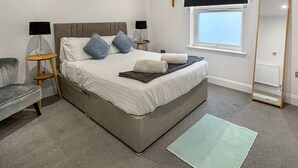 A bedroom with a bed, bedside tables, a mirror, a window, and a carpet.