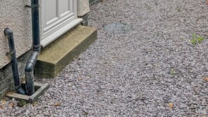 A residential property with a gravel driveway, a wooden bench, and a brick wall in the background.