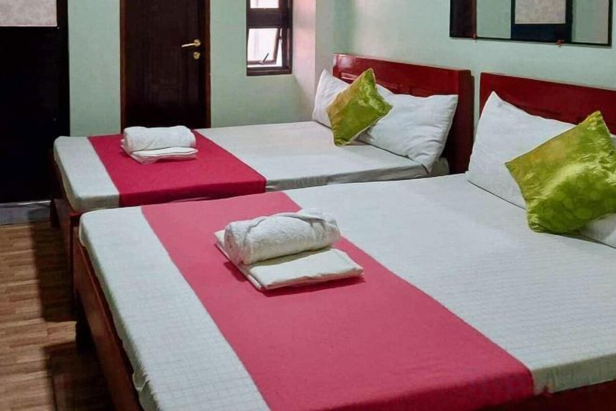 A hotel room with two single beds, each with a red bedspread and white pillows.