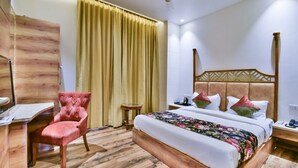 A hotel room with a wooden floor, a bed with a floral bedspread, a red armchair, a small round table, and a ceiling fan. - HOTEL RV GOLDEN (Amritsar)