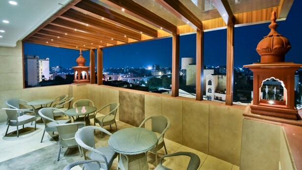 A rooftop terrace with wicker furniture and a view of the city at night. - HOTEL RV GOLDEN (Amritsar)