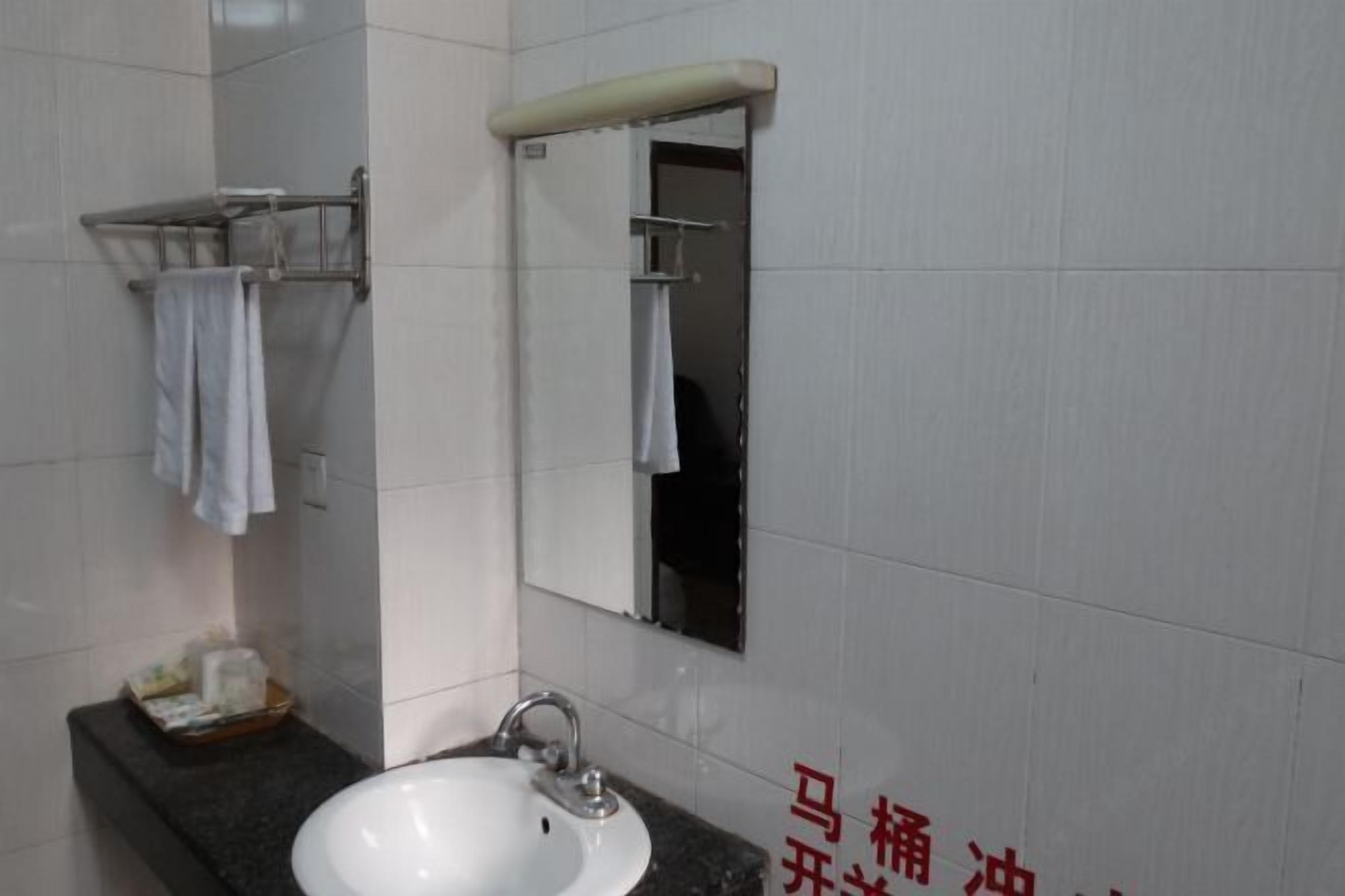 Un baño con un lavamanos blanco, un espejo y un perchero para toallas.