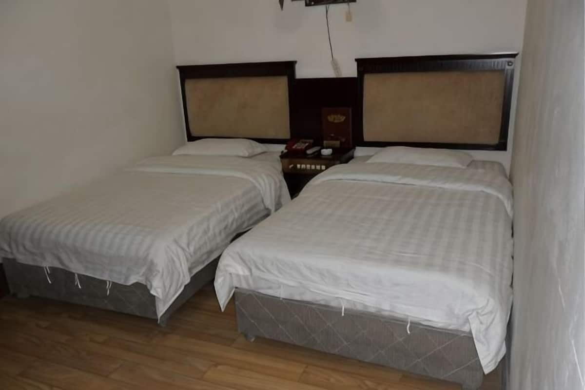 Een kamer met twee eenpersoonsbedden, houten vloer en nachtkastje met telefoon.