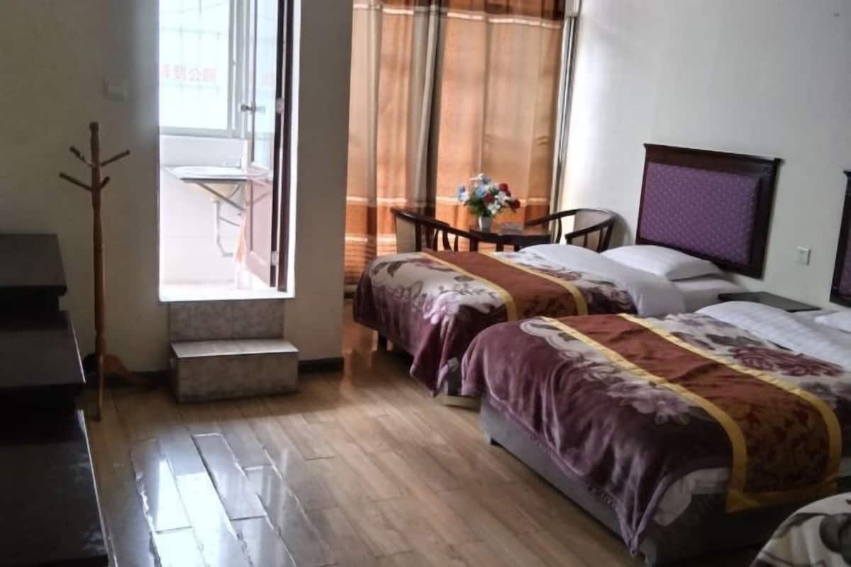 Een hotelkamer met twee bedden, een tafeltje met een bloemenvaas, een stoel en een raam met gordijnen.