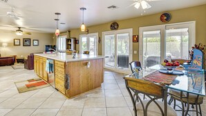 A spacious kitchen with a central island, large windows, and a dining area with a glass table. - Near Surprise Stadium! Home w/ Pet-Friendly Yard (Sun City West)