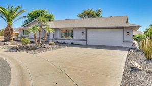 A single-story house with a garage, palm trees, and a well-maintained driveway. - Near Surprise Stadium! Home w/ Pet-Friendly Yard (Sun City West)