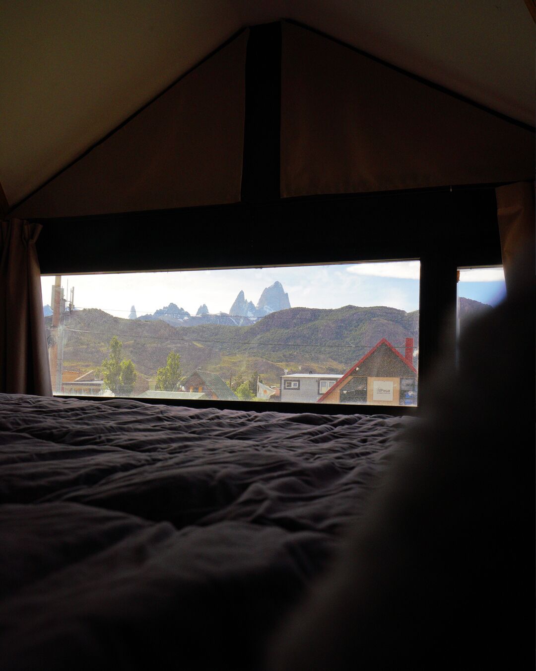 A tented room with a bed and a view of a mountainous landscape and a small building.