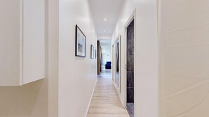 Een hal met ingekaderde foto’s aan de wand, een blauwe bank in de verte en een combinatie van lichte en donkere vloerbedekking.