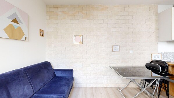 A modern living space with a blue sofa, a glass-top table, and a brick-patterned wall.