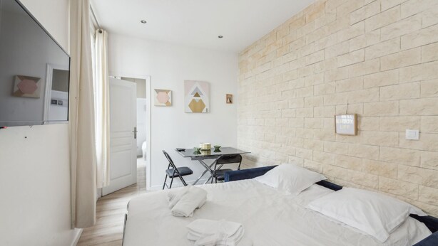 Een slaapkamer met een bed, een bureau en een stoel. Een witte muur met een baksteenstructuur en een deur die naar een andere kamer leidt.