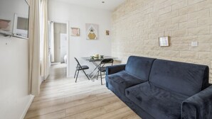 Een moderne woonkamer met een donkerblauwe bank, een eettafel met stoelen en een keuken in de achtergrond.