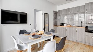 Et moderne køkken med grå skabe, en indbygget ovn og et spiseområde med et bord dækket til fire personer.