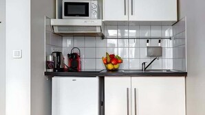 Eine kompakte Küche mit weißen Schränken, einer Mikrowelle, einem Spülbecken und einem kleinen Kühlschrank.