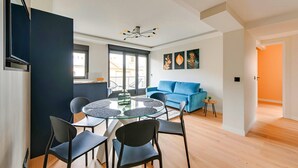 A modern living room with a round glass table, black chairs, a blue sofa, and a ceiling light fixture.