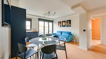 A modern living room with a round glass table, black chairs, a blue sofa, and a ceiling light fixture.