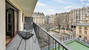 Un balcón con vistas a un paisaje urbano, que incluye una piscina y una silla.