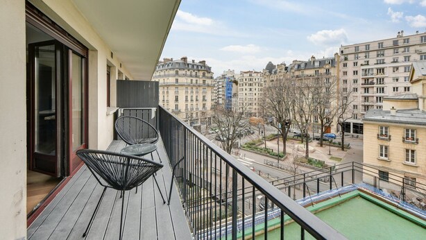 A balcony with a view of a cityscape, featuring a pool and a chair.