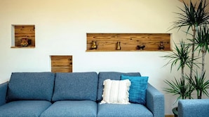 Un soggiorno moderno con un divano blu, mensole a parete in legno e un'alta pianta.