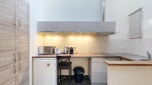 Una kitchenette compacta con estufa integrada, tostadora, hervidor y un cesto de basura.