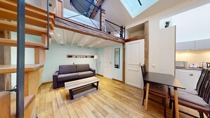 Un espacio habitable estilo loft con entrepiso, un sofá, una mesa de comedor y una zona de cocina.