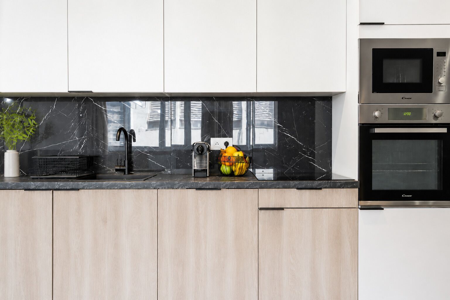Een moderne keuken met een zwarte marmeren aanrecht, een spoelbak, een fruitschaal en twee inbouwovens.