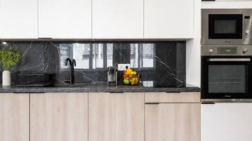 Een moderne keuken met een zwarte marmeren aanrecht, een spoelbak, een fruitschaal en twee inbouwovens.