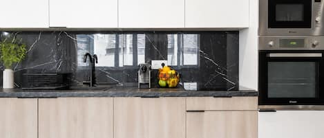 Une cuisine moderne dotée d’un plan de travail en marbre noir, d’un évier, d’un panier à fruits et de deux fours encastrés.