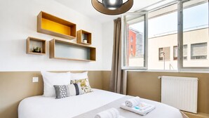 A hotel room with a bed, two side tables, a window with a view of buildings, and a radiator.