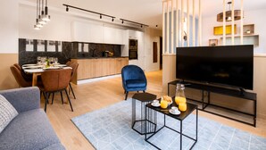 A modern living room with a sofa, a dining area with a table and chairs, a kitchen with a marble backsplash, and a TV on a stand.
