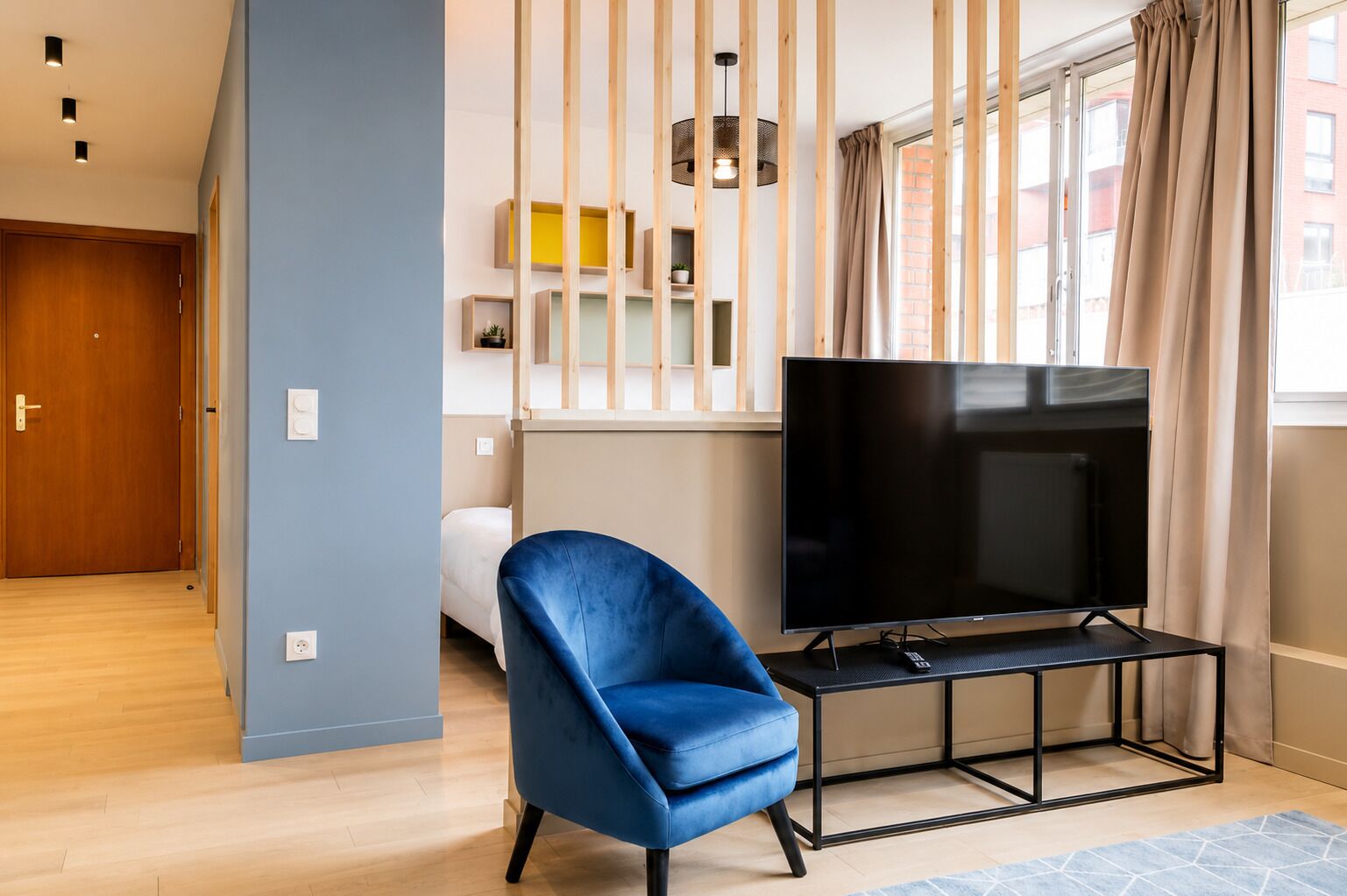 Een moderne woonkamer met een televisie, een blauwe stoel en een houten vloer.
