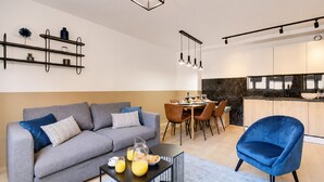 A modern living room with a grey sofa, a blue armchair, and a dining area with a table set for four.