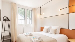 A neatly made bed with a patterned bedspread, a set of towels, and a ladder against the wall. - TBS 87 - Fabulous apartment in Paris (Paris)