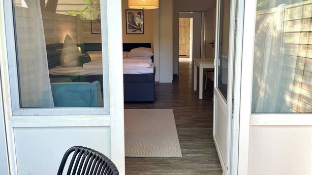 A hotel room with a bed, a desk, and a chair. There is a window on the left side and a door leading to another room. - Compact and comfortable, Kompakt und Komfortabel (Bad Rothenfelde)