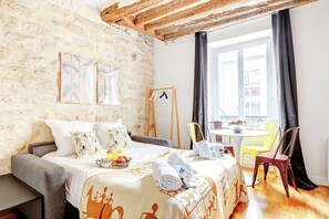 Una habitación acogedora con una cama, una mesita con sillas, una ventana con cortinas y obras de arte en la pared.