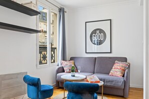 A living room with a grey sofa, two blue armchairs, a small round table with a bottle and glasses, and a framed quote on the wall. - TheBlueStay 238- Beautiful Apartment in Paris 17 (Paris)